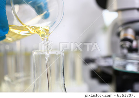 Scientist hand wearing protective gloves pouring some yellow liquid at laboratory 63618073