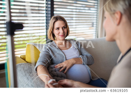 Healthcare worker with IV drip examining pregnant woman indoors at home. Healthcare worker with IV drip examining pregnant woman indoors at home. 63619105