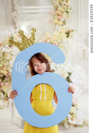A girl in a yellow dress holds a large number 6.With a Golden crown. The Princess birthday party. A girl in a yellow dress holds a large number 6.With a Golden crown. The Princess birthday party. 63620349