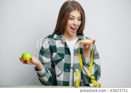Cute woman makes a choice between healthy and harmful food Cute woman makes a choice between healthy and harmful food 63623751
