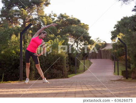 Fit caucasian middle aged woman do warming up on the footpath outdoor in summer among greenery, selective focus. 63626075