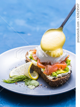 Morning and breakfast concept - Preparation of sandwich with salmon, spoon is pouring sauce on it. 63629547