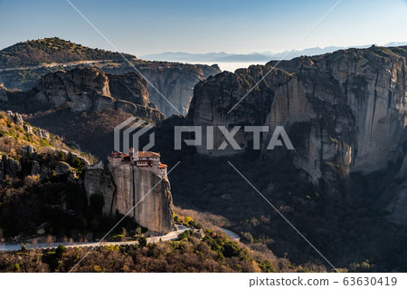 Aerial view of monastery Rousanou and breathtaking picturesque valley and landmark canyon of Meteora at sunset, Kalambaka, Greece, shadows, twisted road, bridge Aerial view of monastery Rousanou and breathtaking picturesque valley and landmark canyon of Meteora at sunset, Kalambaka, Greece, shadows, twisted road, bridge 63630419