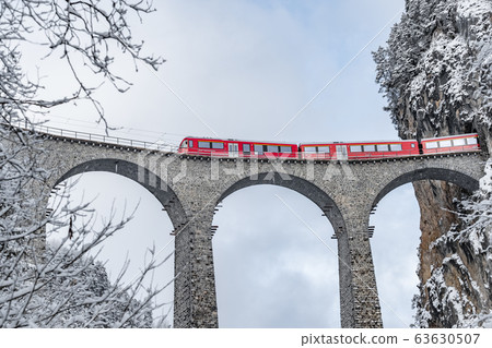 The Landwasser Viaduct with famous train of red color at winter time, landmark of Switzerland, snowing, Glacier express 63630507
