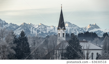 Aerial view of the small cozy german town at the mountain bottom at sunrise in a winter season, Halblech city, Germany, Bavaria, Branches of trees are covered with hoarfrost, sunny weather Aerial view of the small cozy german town at the mountain bottom at sunrise in a winter season, Halblech city, Germany, Bavaria, Branches of trees are covered with hoarfrost, sunny weather 63630518