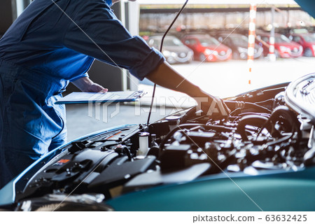 Car mechanic holding clipboard and checking to 63632425
