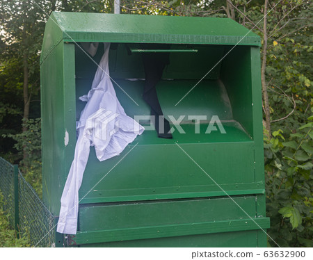 green container for clothes, clothes sticking out of the container green container for clothes, clothes sticking out of the container 63632900