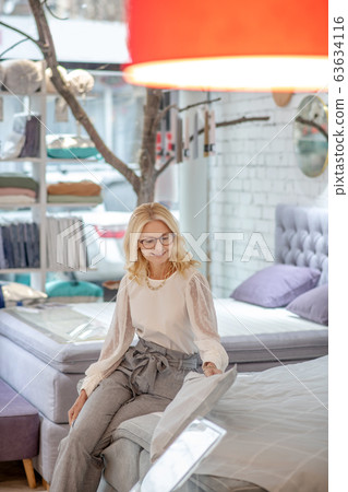 Blond-haired woman sitting on the bed in the store. 63634116