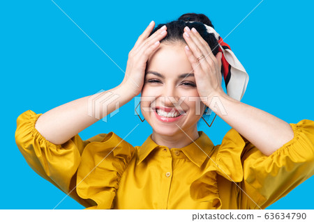 Young woman in a mustard dress holding her head and smiling 63634790