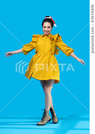 Young woman in a mustard dress standing with legs crossed 63634806
