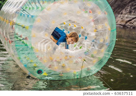 Cute little boy, playing in Zorb a rolling plastic cylinder ring with a hole in the middle on the 63637511