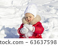 Winter activities for children. A little girl is trying to make a snowball. She is dressed in a bright red coat with a white hat and scarf and mittens. Wonderful pastime in the winter. Portrait 63637598