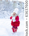 Enjoyment in the winter season. A beautiful little girl in a red coat and white hat with a scarf runs along a snowy path in a winter park. Smile and children's joy on the face. Great holidays. Snow 63637600