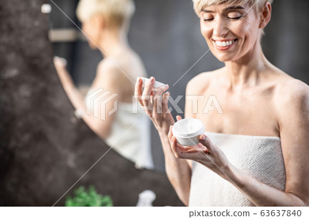 Smiling Woman Opening Facial Cream Standing In Bathroom At Home Smiling Woman Opening Facial Cream Standing In Bathroom At Home 63637840