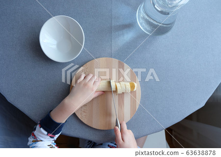 a 6 year old child cutting a ripe banana on grey 63638878