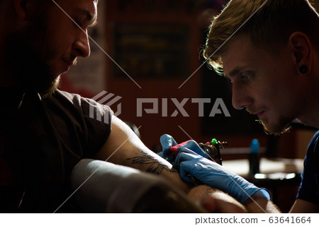 Professional tattoo artist makes a tattoo on a man's hand. 63641664