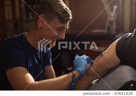 Professional tattoo artist makes a tattoo on a man's hand. 63641826