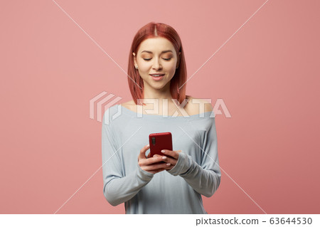 Smiling young woman with phone in her hands standing in studio 63644530