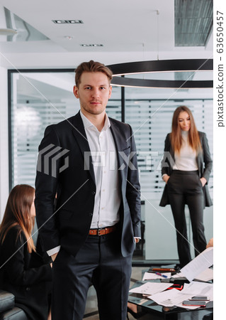 Portrait of successful manager looking at camera on the background of talking people Portrait of successful manager looking at camera on the background of talking people 63650457