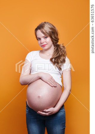 Pregnant happy woman touching her belly on yellow background Pregnant happy woman touching her belly on yellow background 63651576