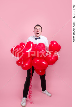 Elegant young man with heart shape air balloons on pink background. Valentine's Day. Elegant young man with heart shape air balloons on pink background. Valentine's Day. 63651783