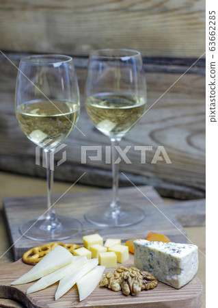 two glass of white wine with cheese board on rustic background with various cheese,blue cheese,gauda and nuts and snacks 63662285