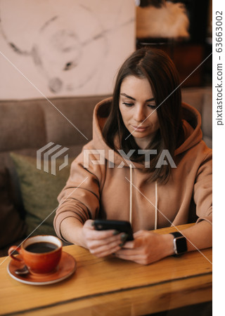 Portrait of young handsome woman sitting in coffee shop at wooden table 63663002