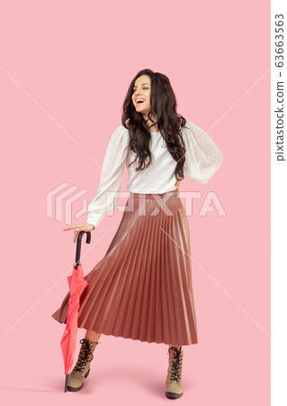 Young pretty dark-haired woman in a pleated skirt holding a red umbrella Young pretty dark-haired woman in a pleated skirt holding a red umbrella 63663563
