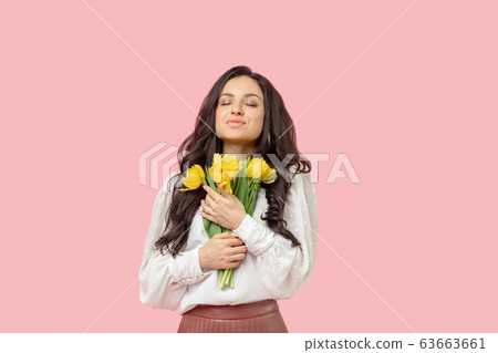 Young pretty dark-haired woman holding yellow flowers and feeling pleased 63663661