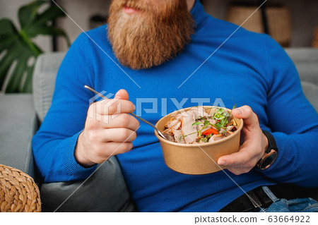 A man eats at home on the couch. Man in a blue 63664922