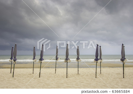 Many umbrellas on the sandy beach Background sea and black rain clouds. 63665884