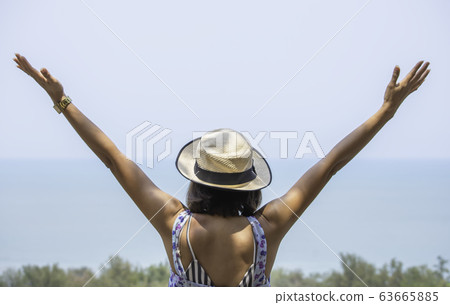 The image behind Asian women raise their arms and wear a hat  background sea. 63665885