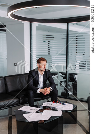 Handsome stylish confident businessman in a smart suit sitting on a sofa in the office. 63668215