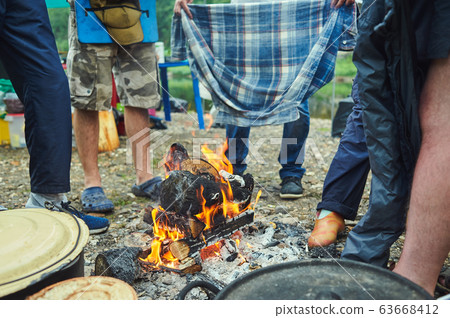 Wet tourists hike around the campfire and dry their clothes. Soaked in the rain in forest 63668412