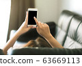 women using blank screen smartphone on black sofa at home with clipping path 63669113