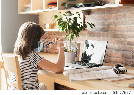 Child girl in a medical mask performs lessons through a digital laptop. Online education during an epidemic. 63672637