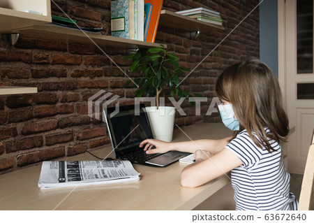 Child girl in a medical mask performs lessons through a digital laptop. Online education during an epidemic. 63672640