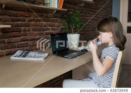 Child girl in a medical mask performs lessons through a digital laptop. Online education during an epidemic. 63672649