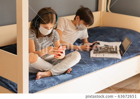 Children boy and a girl in a medical mask carry out lessons through laptop. Online education during a pandemic epidemic. Children boy and a girl in a medical mask carry out lessons through laptop. Online education during a pandemic epidemic. 63672651