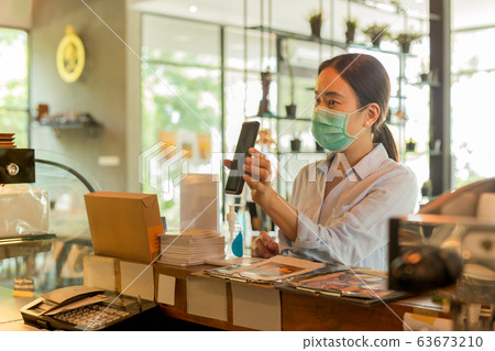 Woman customer with protective mask paying bill by cell phone in cafe. 63673210