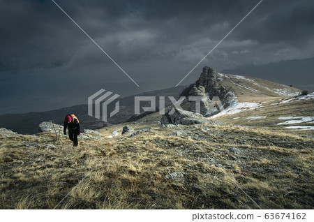 Female hiker with an orange backpack goes up the mountain 63674162