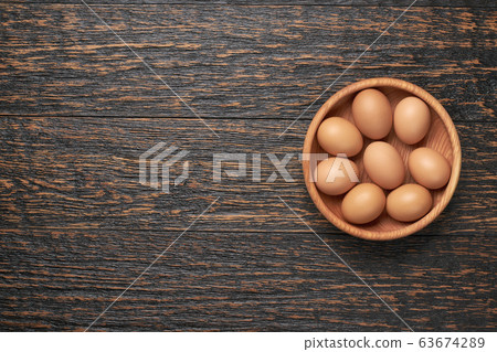 Organic chicken eggs in a wooden bowl on a black 63674289