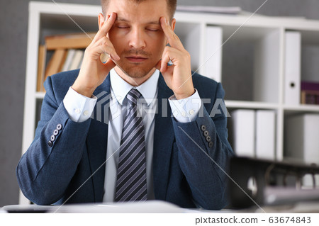 A man experiences stress and a headache in the workplace A man experiences stress and a headache in the workplace 63674843