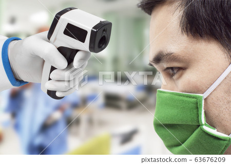 Medical infrared thermometer in a hand of the doctor measuring the temperature of the male patient. Medical infrared thermometer in a hand of the doctor measuring the temperature of the male patient. 63676209