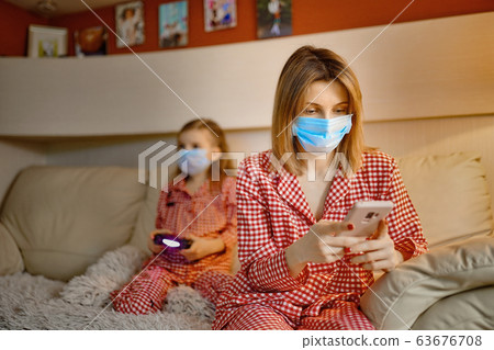 Woman with Little kid at home isolation auto quarantine wearing face mask with smart phone for reading information about COVID-19 63676708