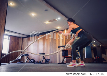 Caucasian fit woman dressed in sportsoutfit posing with battle ropes at gym 63677102