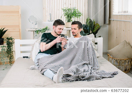Happy gay couple together on bed at home. Gay Couple Love Home Concept Happy gay couple together on bed at home. Gay Couple Love Home Concept 63677202