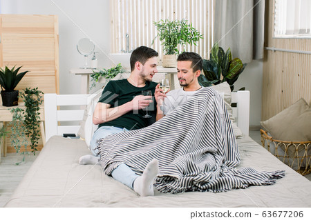 Happy gay couple together on bed at home. Gay Couple Love Home Concept Happy gay couple together on bed at home. Gay Couple Love Home Concept 63677206