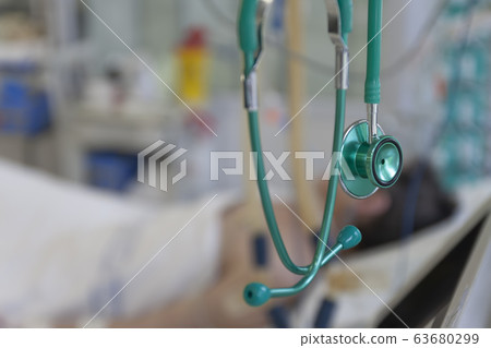 Green stethoscope, on background patient  connected to medical ventilator in ICU in hospital, a place where can be treated patients with pneumonia caused by coronavirus covid-19. 63680299