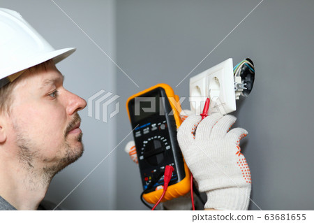 Electrician in helmet measures level electricity 63681655
